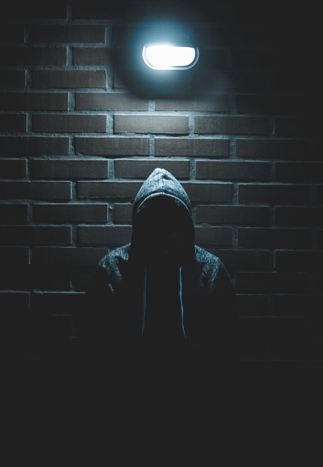 Hooded figure standing in front of brick wall